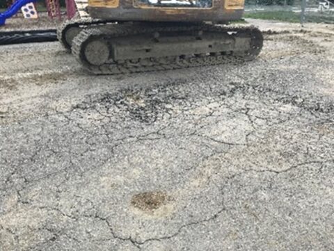 Cracked asphalt beside excavation equipment.