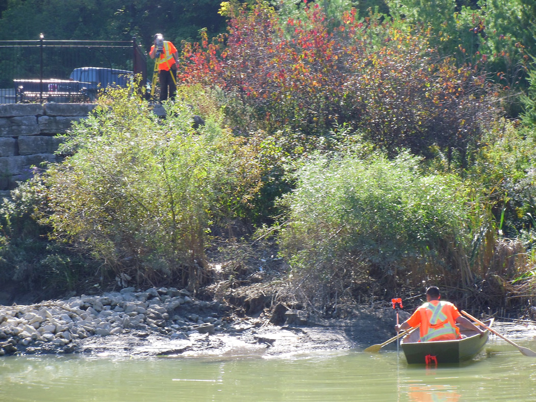 Figure 2. Field crew conducting a bathymetric survey of Pond 91 using a standard disk, rod and total station method. One crew member is on the shore with the survey rod, and the other is in a boat in the water taking measurements.