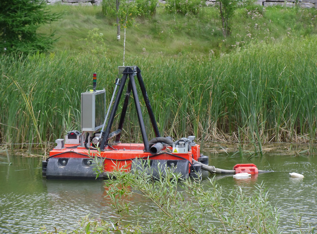 Figure 5. Hydraulic mini dredge floating in the pond, equipped with hoses, a control panel, and support framework.
